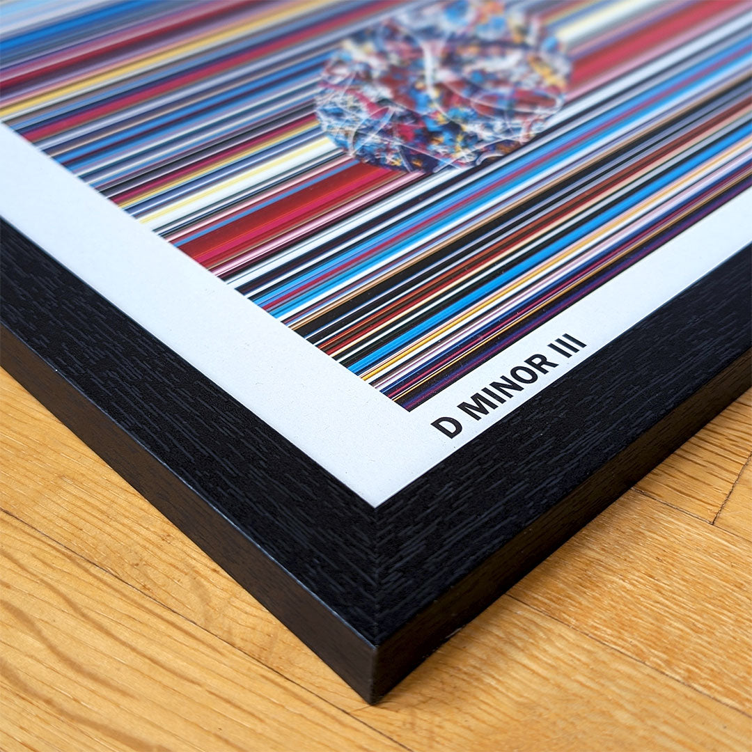 Close up of the corner detail of a black framed multicolour music art print lying on an oak floor