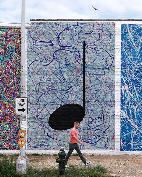 Street Art Mural on a high brick wall in a city street with a man walking past