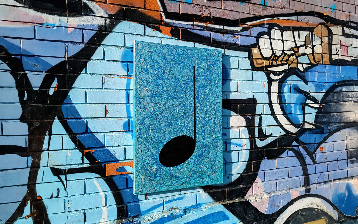 A turquoise Music Graffiti canvas painting hanging on a street art mural wall
